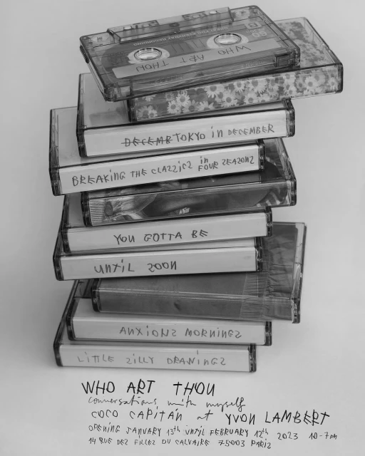 Stack of audio cassette tapes with handwritten labels and a poster announcing an art exhibition by Coco Capitán at Yvon Lambert.