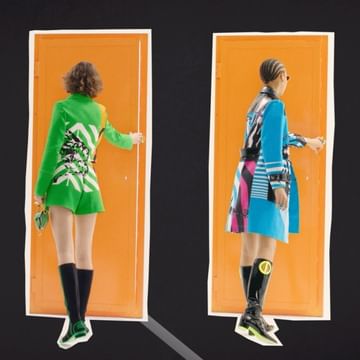 Two fashion models in coordinated outfits stand facing away from the camera in front of separate orange doors on a black background.