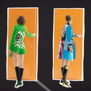 Two fashion models in coordinated outfits stand facing away from the camera in front of separate orange doors on a black background.