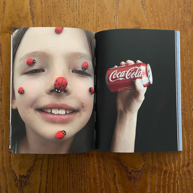 Open magazine spread with child's face decorated with ladybug stickers on the left and a hand holding a Coca-Cola can on the right.