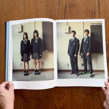 Open book featuring two school-age girls and boys in uniform posing indoors, photographed on the pages of the book.