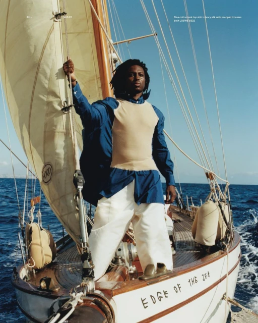 Adult male sailing on a white sailboat on the ocean. The sky is clear and blue, and the boat has brown wooden trim.