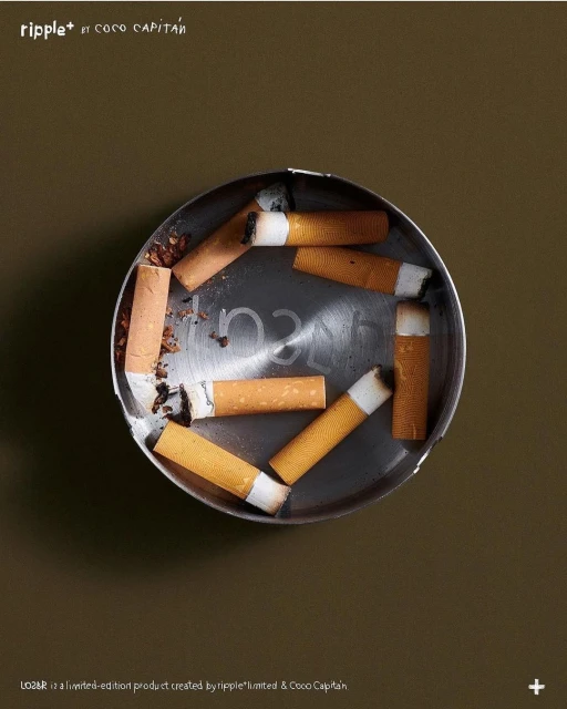 Overhead shot of cigarette butts in a metallic ashtray, set against a solid brown background, creating a still life composition.