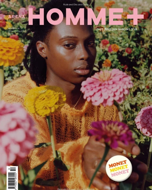 Arena Homme+ cover featuring a Black male model with dreadlocks, wearing an orange sweater, surrounded by pink, yellow, and purple flowers.