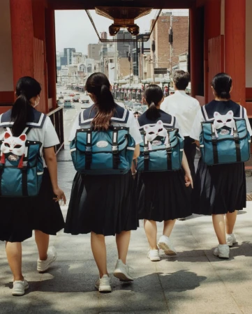 A group of students in school uniforms walk away from the camera, entering a city street through a red wooden temple gate.
