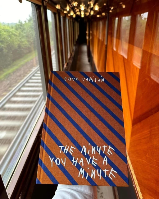 Book titled 'The Minute You Have A Minute' held inside a train car, view looking down the length of the train.
