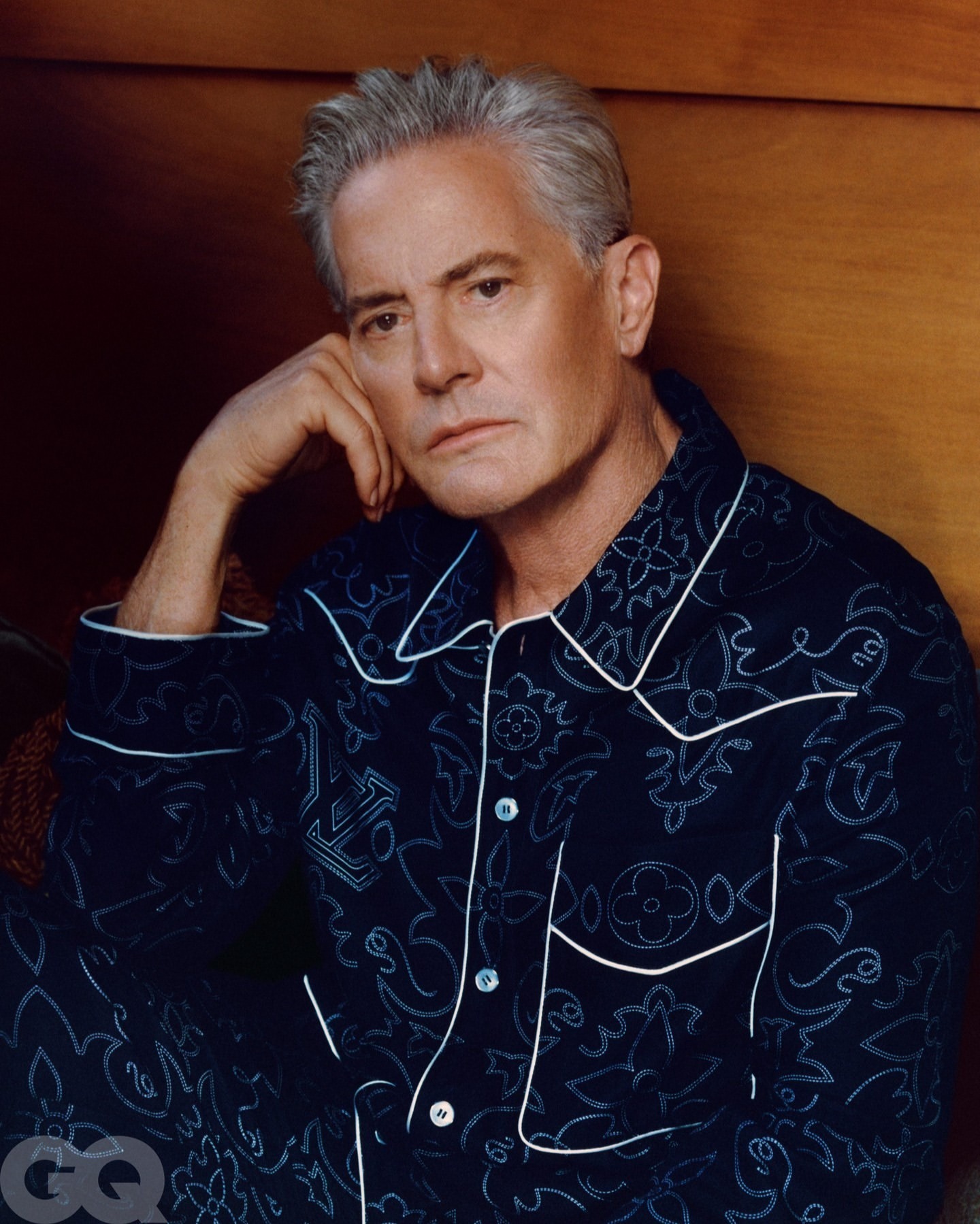 Portrait of an adult male wearing a patterned pajama set, resting his head on his hand with a serene expression.