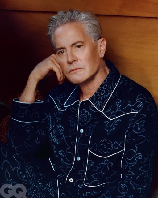 Portrait of an adult male wearing a patterned pajama set, resting his head on his hand with a serene expression.