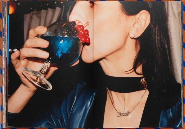 Close-up portrait of a woman drinking from a large blue cocktail garnished with berries, photographed by Coco Capitan.