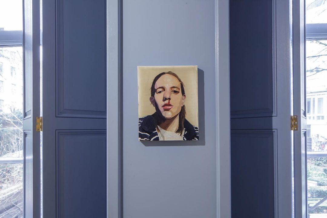 Painted portrait of a young adult with long hair and a striped jacket on a gray wall between two blue paneled doors.