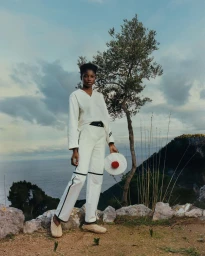Model standing outdoors wearing white apparel holding a round white bag with red detail, shot by Coco Capitan.