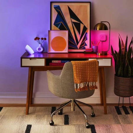 Desk setup featuring a mid-century modern desk with decor, including lamps, framed art, and a chair, set against a neutral wall.