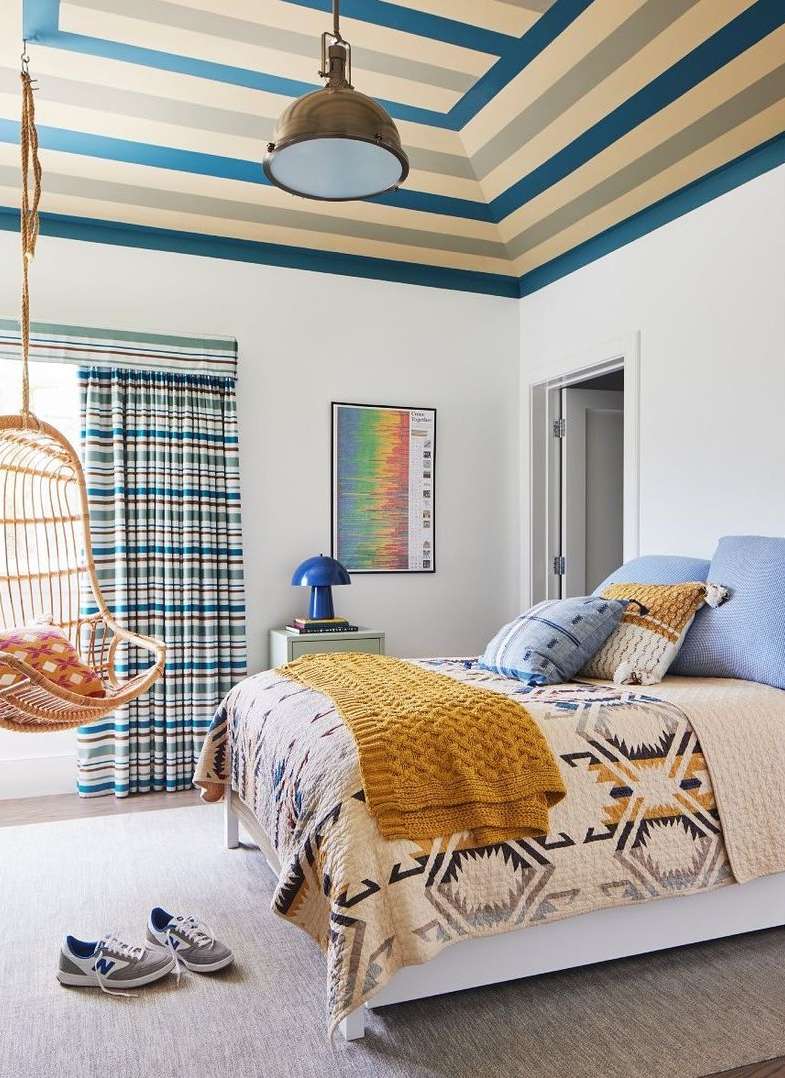 Bedroom featuring a bed with patterned bedding and throw blanket, a hanging chair, and a blue lamp on a side table.