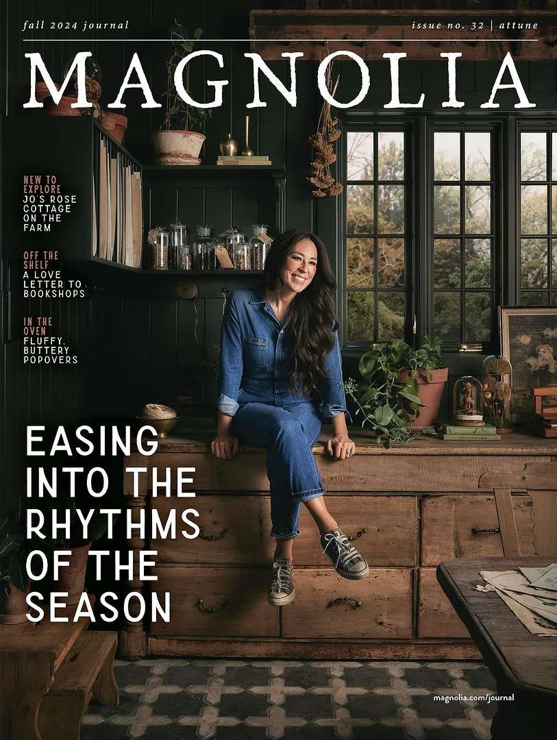 Magazine cover featuring a woman in denim sitting on a wooden dresser, with shelves, windows, and plants in the background.