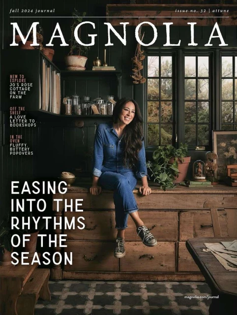 Magazine cover featuring a woman in denim sitting on a wooden dresser, with shelves, windows, and plants in the background.