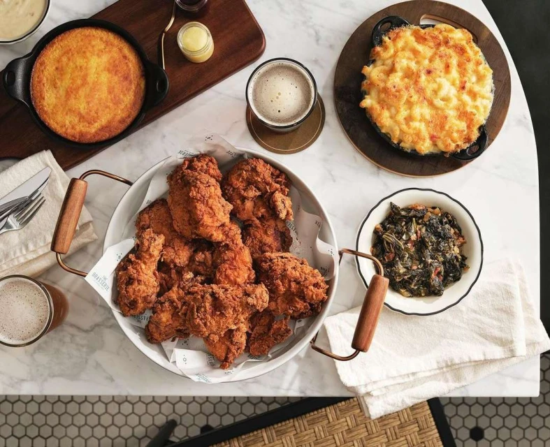 Overhead view of a table filled with Southern comfort food, including fried chicken, mac and cheese, cornbread, and collard greens, plus beer.