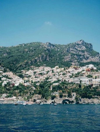 Picturesque view of the Amalfi Coast hillside with white buildings and green foliage, overlooking the blue sea under a clear sky.