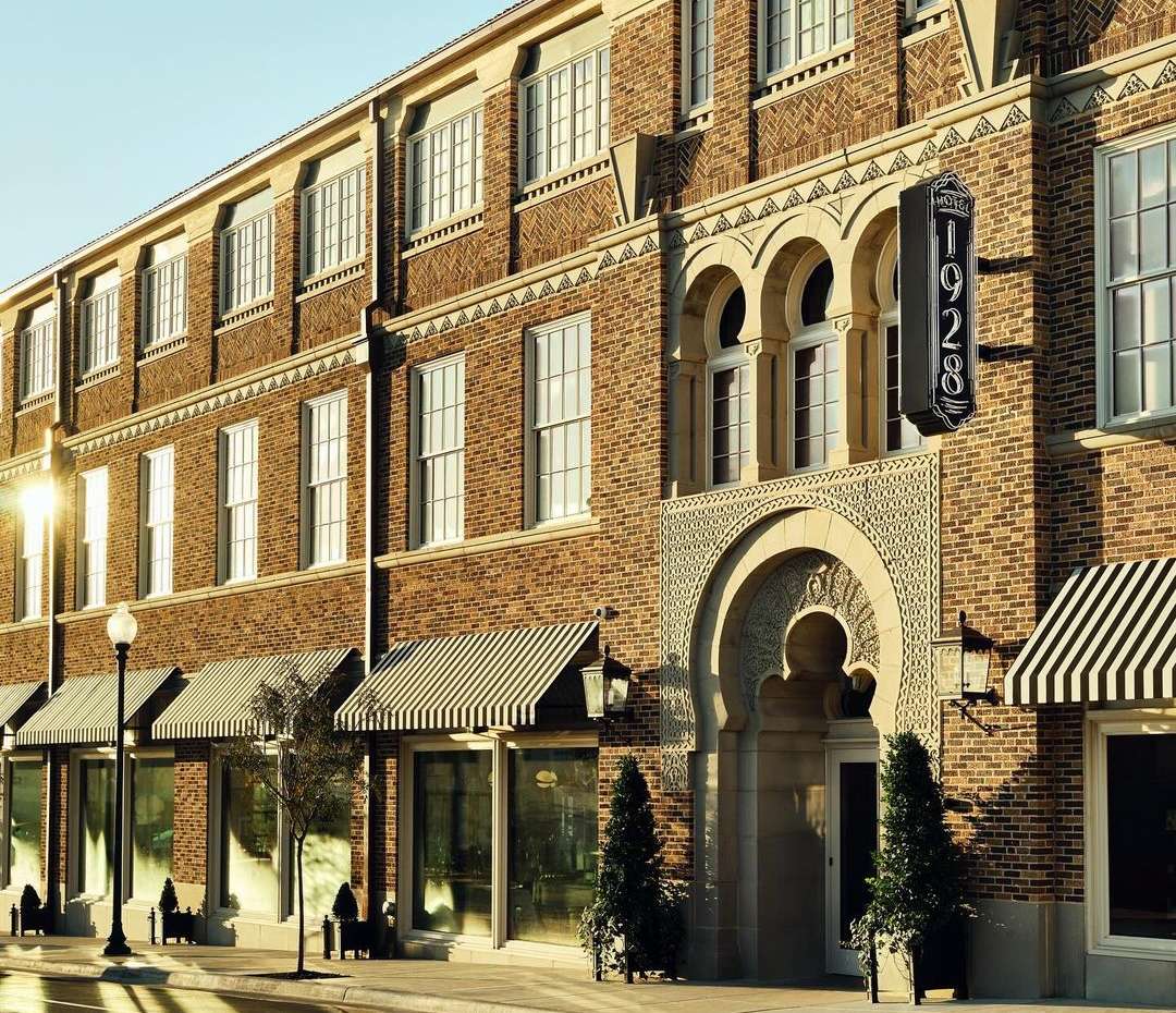Exterior of a three-story brick building with awnings and a vertical '1928' sign, showcasing its architectural details and inviting entrance.