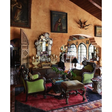 Ornate living room featuring vintage furniture, paintings, and decorative objects, showcasing an interior design aesthetic with rich textures.