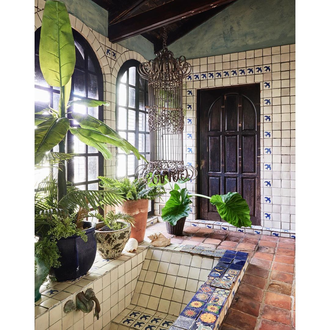 Indoor tropical-style bathroom featuring green potted plants, tile walls and floors, and a wrought-iron chandelier, creating a serene space.