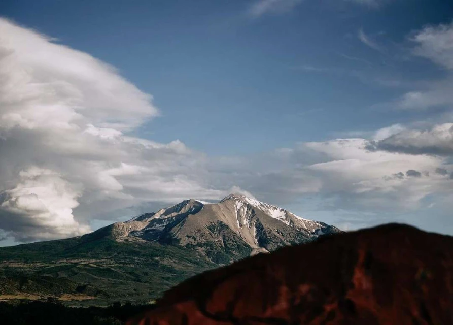 Scenic view of a snow-capped mountain range under a blue sky with puffy white clouds in the background, capturing nature's beauty.