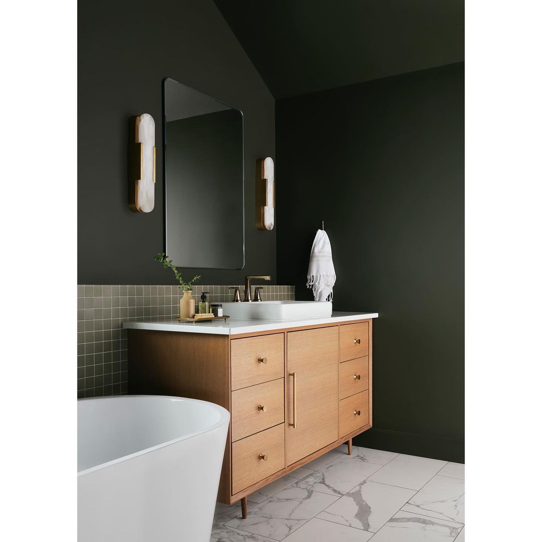 Bathroom interior featuring a wood vanity with a white countertop, a rectangular sink, a frameless mirror, and sconce lighting.