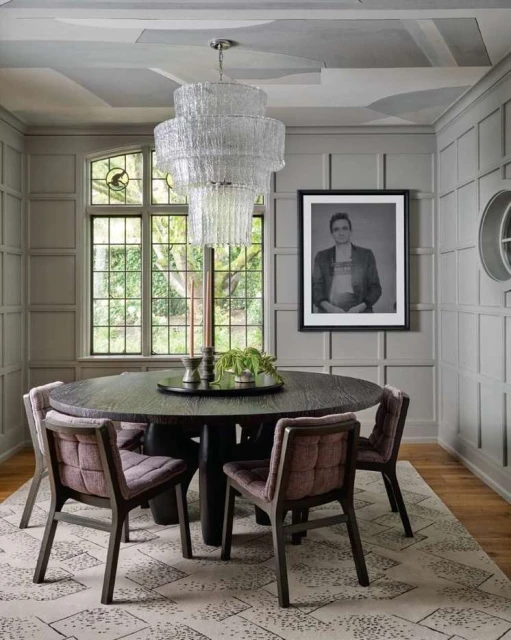 Interior of a dining room featuring a dark wood table, upholstered chairs, and a tiered glass chandelier; framed portrait on the wall.