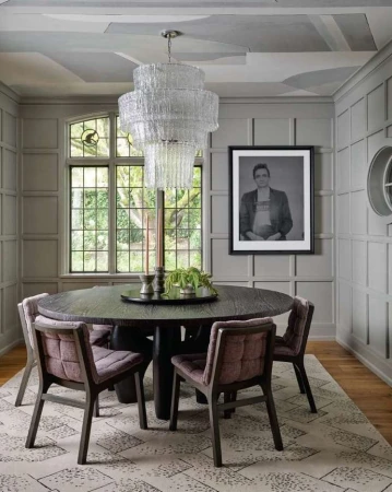 Interior of a dining room featuring a dark wood table, upholstered chairs, and a tiered glass chandelier; framed portrait on the wall.