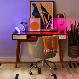 Mid-century modern wooden desk with artwork, lamp, and a grey office chair with an orange throw blanket by Cody Ulrich