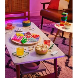Colorful board game and bowls of snacks set on a marble coffee table in a cozy living room with ambient lighting
