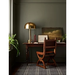 Wooden desk with brass table lamp and leather armchair against dark olive wall photographed by Cody Ulrich