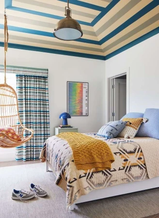 Bright child bedroom with striped ceiling, hanging rattan chair, and patterned bedspread photographed by Cody Ulrich