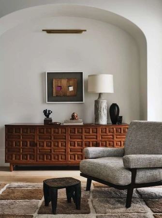 Interior shot featuring a grey upholstered armchair, wooden credenza, and arched wall in a living room by Cody Ulrich