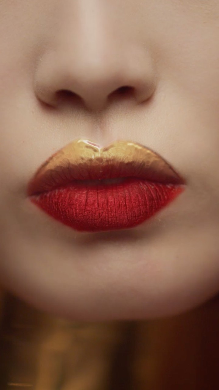 Close-up of an adult woman's face features, showcasing red lipstick with a gold-painted upper lip against a soft blurred background.
