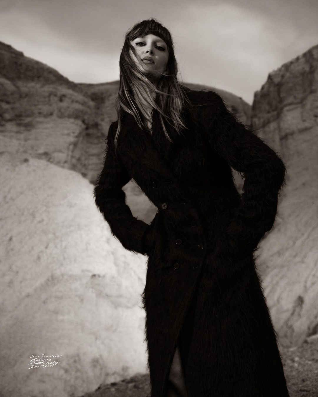 Model in a long textured dark coat standing in a rocky landscape captured from a low angle by photographer Cole Sprouse