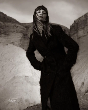 Model in a long textured dark coat standing in a rocky landscape captured from a low angle by photographer Cole Sprouse