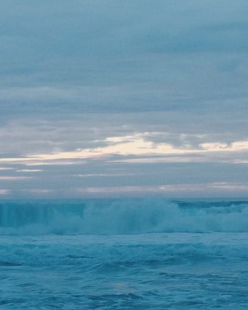 Ocean wave crests and breaks under a cloudy sky in a serene seascape, showcasing the power and beauty of the natural world.