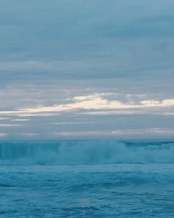 Ocean wave crests and breaks under a cloudy sky in a serene seascape, showcasing the power and beauty of the natural world.