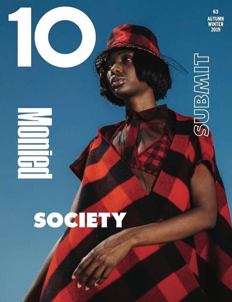 Magazine cover featuring a black woman in a red and black plaid outfit with matching hat against a blue sky background, vertical orientation.