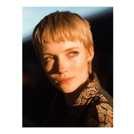 Portrait of a young white woman with short blonde hair and patterned collar shirt under warm lighting photographed in London by Cole Sprouse.