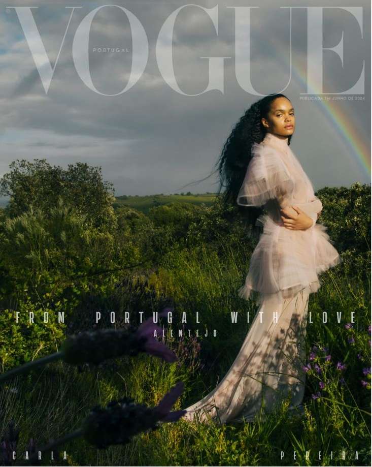Vogue Portugal cover features a woman in a flowing dress standing in a field with a rainbow in the background, artistic fashion portrait.