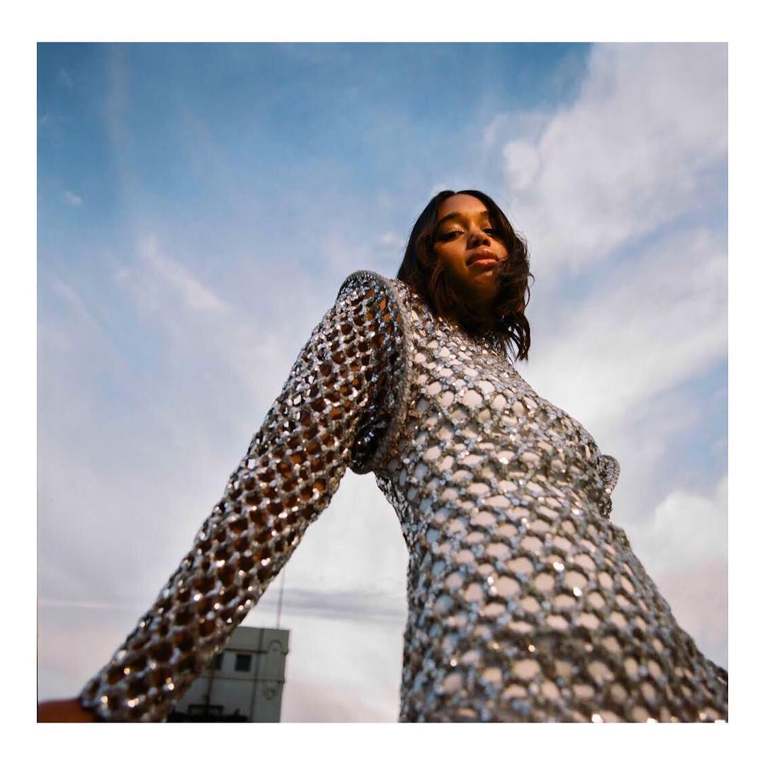 Eye-level view of an adult female in a silver-sequined dress against a cloudy sky, showcasing fashion and outdoor style in an urban setting.