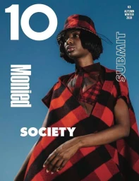 Model wearing a red and black plaid poncho and matching bucket hat against a solid blue sky background
