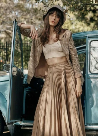 Woman in a plaid blazer and pleated skirt leaning against a vintage blue car in Los Angeles by Colette De Barros.