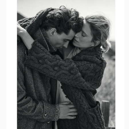 Black and white portrait of a man and woman embracing outdoors wearing textured knitwear.