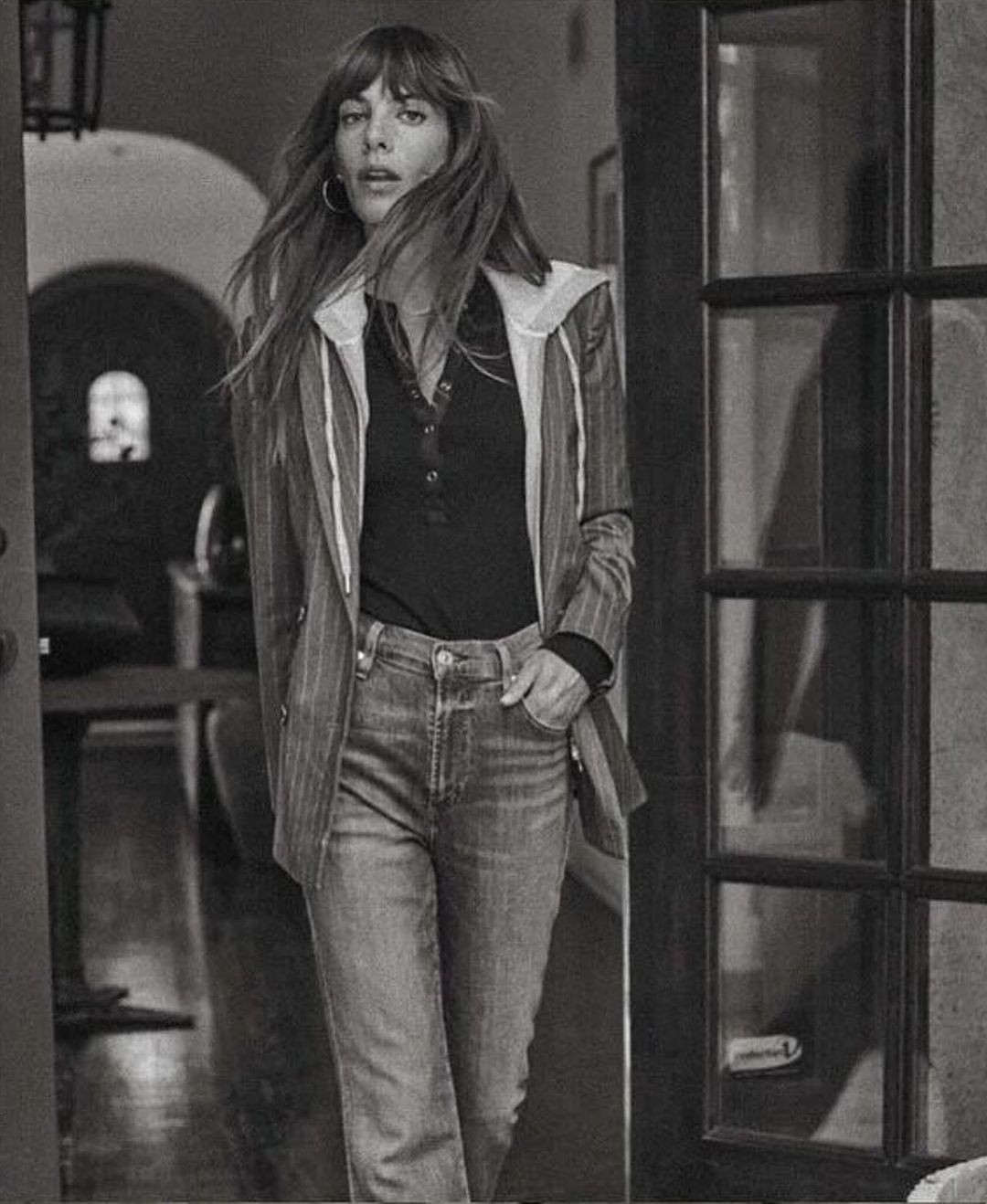 Monochrome portrait of a woman with long hair wearing a pinstripe blazer and jeans standing in an indoor doorway
