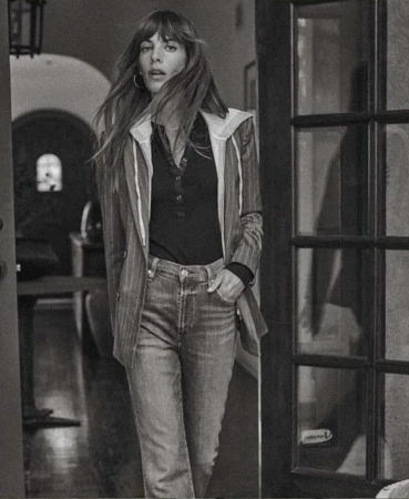 Monochrome portrait of a woman with long hair wearing a pinstripe blazer and jeans standing in an indoor doorway
