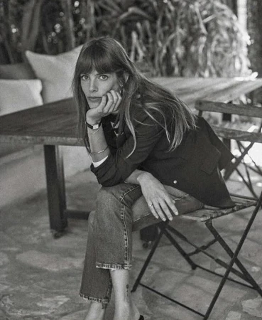 Black and white portrait of a woman sitting on a wooden chair outdoors with her chin resting on her hand.