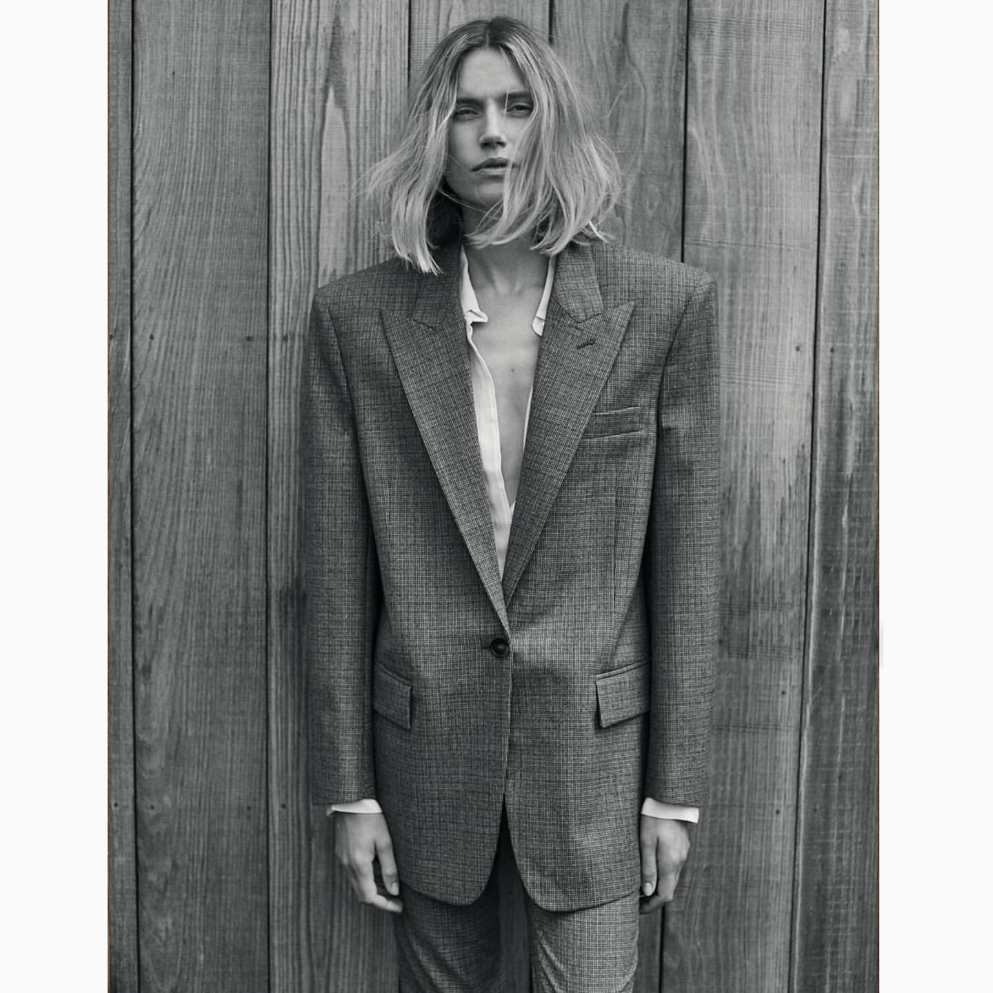 Woman in an oversized gray suit stands in front of a wooden plank wall in a studio, showcasing a blend of fashion and portraiture.