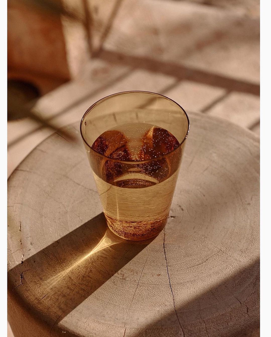 Close-up of a glass of sparkling water on a wooden surface, with sunlight and shadows creating a warm, natural ambiance. Refreshing drink.